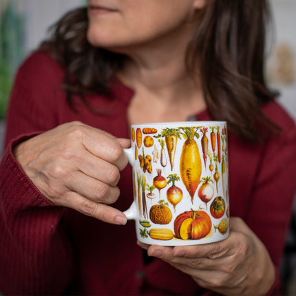 a seated model holds the vegetables mug with the handle in her right hand showing the colorful orange and red vegetable side of the mug