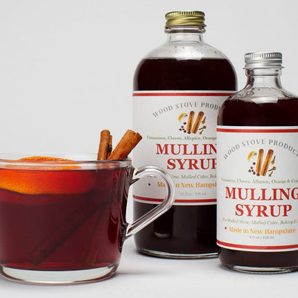 two bottles of mulling syrup next to a clear glass mug filled with a mulled beverage and two cinnamon sticks