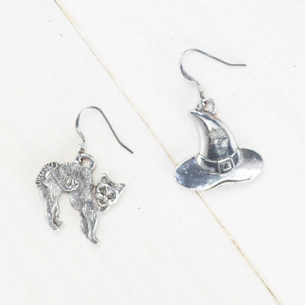 handcrafted pewter witch hat earring, featuring a small stamped star on the hat and a handcrafted pewter cat earring with detailed fur and an arched back, evoking a spooked stance, against a plain white background