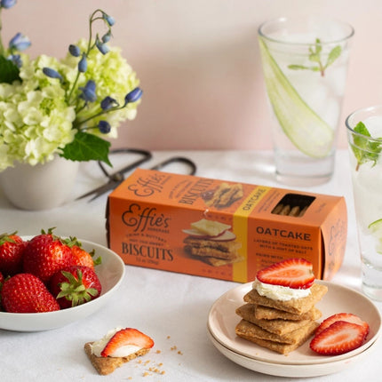 a sweet tabletop spread featuring a box of effie's oatcakes, strawberries, cheese, and a vase with flowers