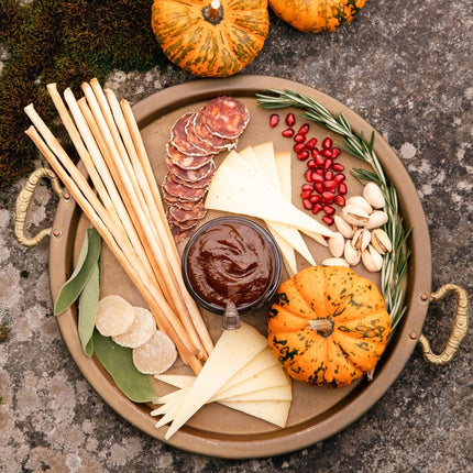an above view of a circular charcuterie board with cheeses, nuts, fruit, and an open jar of pumpkin butter