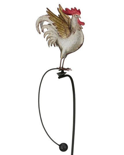 a farther photo of A metal garden stake featuring a colorful rooster with detailed feathers, perched on a rocker that moves in the wind.