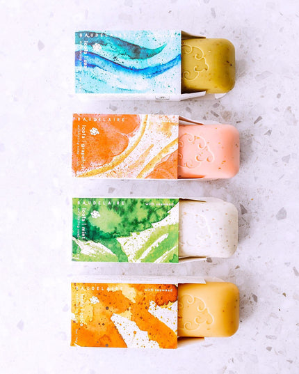 all four scents of the Loofa soaps in a vertical line with each soap peeking out of its package showing both the box design and soap color