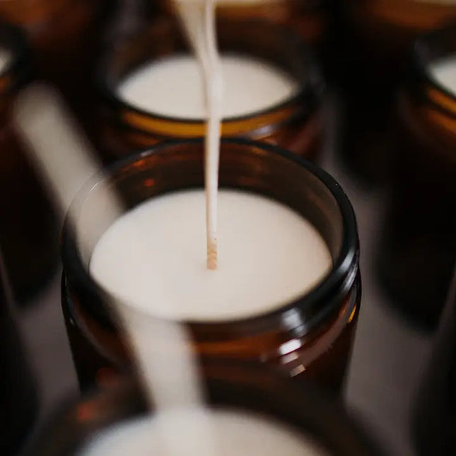 production shot of several candles in their amber glass jars with the lids off revealing the white soy wax and long wicks prior to being cut