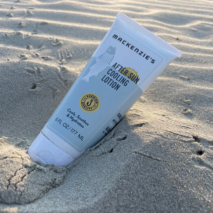 a bottle of after sun cooling lotion nestled in a sand dune with bird footprints on the sand behind it