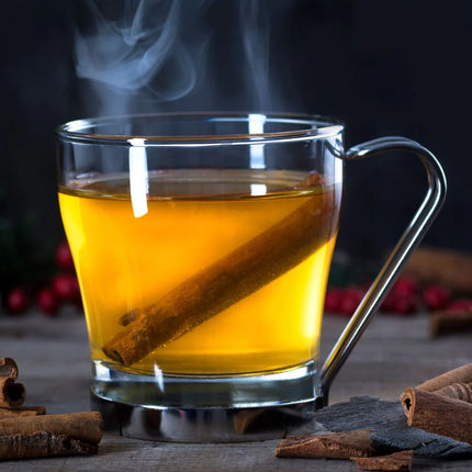 Steaming glass of hot tea with cinnamon sticks on a wooden surface.