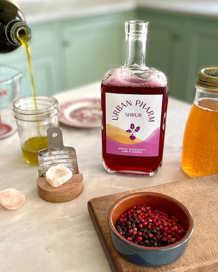 a kitchen counter with a bottle of Apple Rosemary shrub and fresh ingredients
