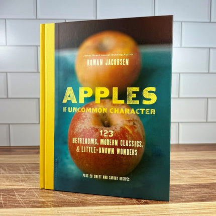 Book titled 'Apples of Uncommon Character' on a wooden surface with a tiled wall background