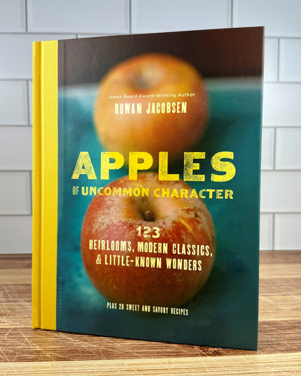 Book titled 'Apples of Uncommon Character' on a wooden surface with a tiled wall background