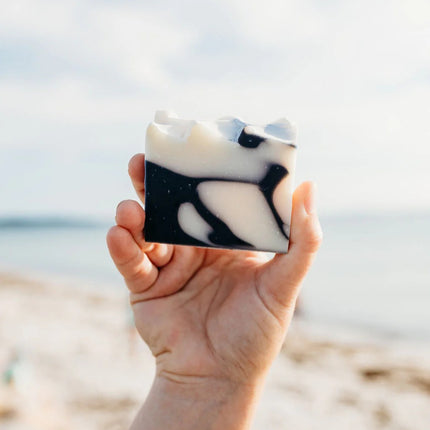 Hand holding a black and white soap bar with a beach background