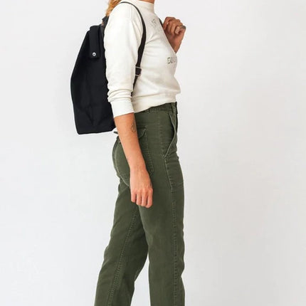 Woman wearing a white sweatshirt, green pants, and brown shoes with a black backpack on a white background