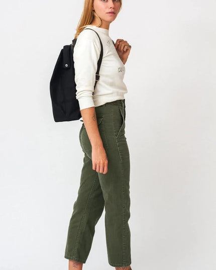 Woman wearing a white sweatshirt, green pants, and brown shoes with a black backpack on a white background