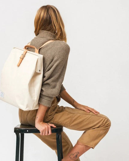Person sitting on a stool wearing a beige backpack against a white background