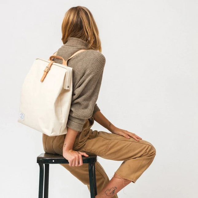Person sitting on a stool wearing a beige backpack against a white background