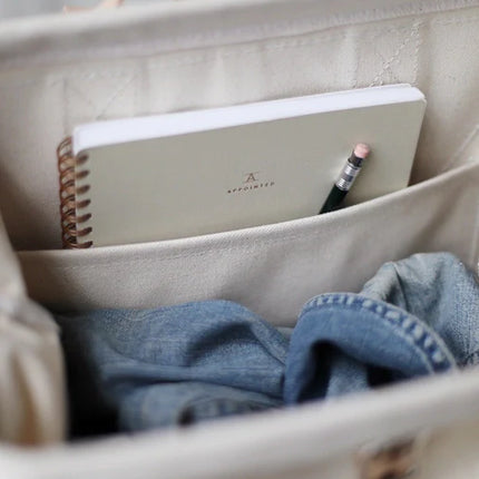 Beige bag with a notebook, pencil, and blue fabric inside