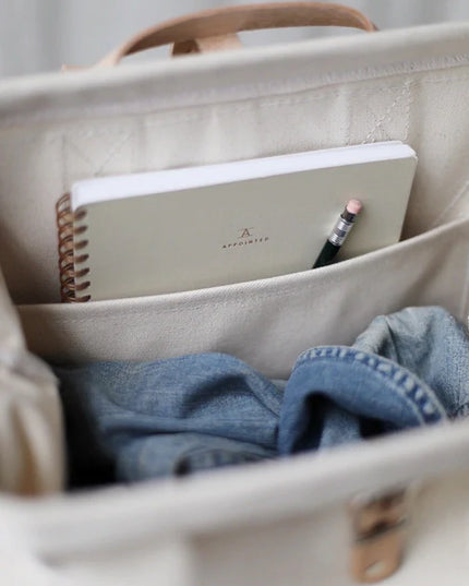 Beige bag with a notebook, pencil, and blue fabric inside