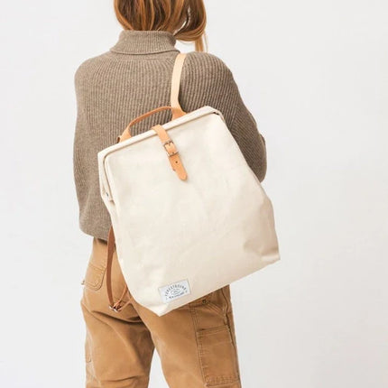 Person wearing a beige tote bag with leather straps on a plain background