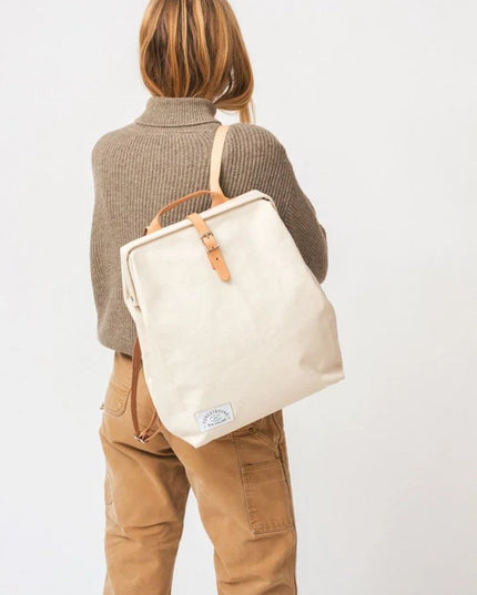 Person wearing a beige tote bag with leather straps on a plain background