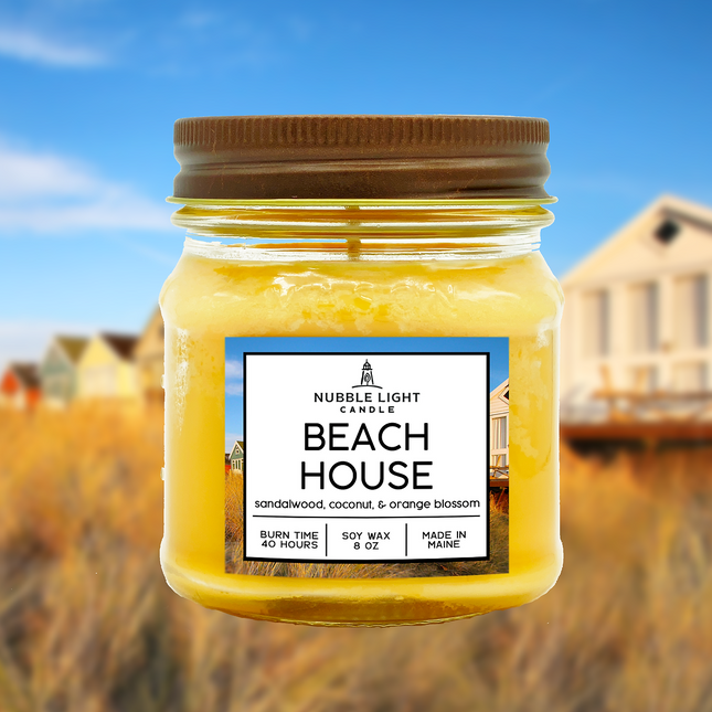 Jar of 'Beach House' scented candle with a blurred beach house background