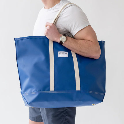 Person holding a blue tote bag with visible branding on a plain background