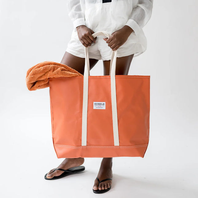 Person holding an orange tote bag with a towel draped over it on a white background