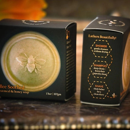 the Bee Soothed soap bar in its packaging showing the honey bee imprint on the bar of soap and suggested uses on the side of the box: Shower, Shampoo, and Shave
