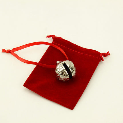 Silver bell with red satin ribbon on a red velvet pouch against a beige background