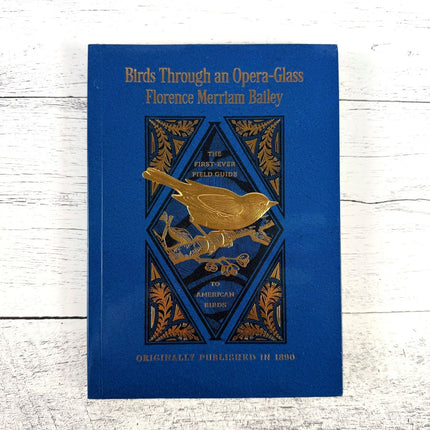 Birds through an Opera Glass book with gold bird illustration on a white wooden surface