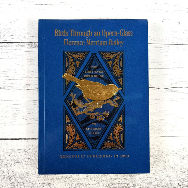 Birds through an Opera Glass book with gold bird illustration on a white wooden surface