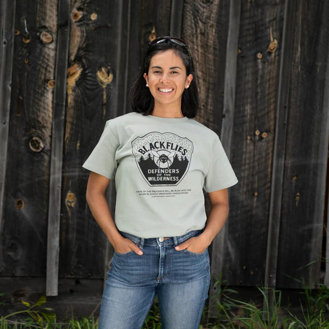 Woman wearing a t-shirt with a blackflys design in front of a wooden wall.