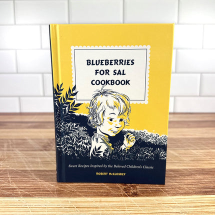 Cookbook titled 'Blueberries for Sal' on a wooden surface with a white tiled wall background