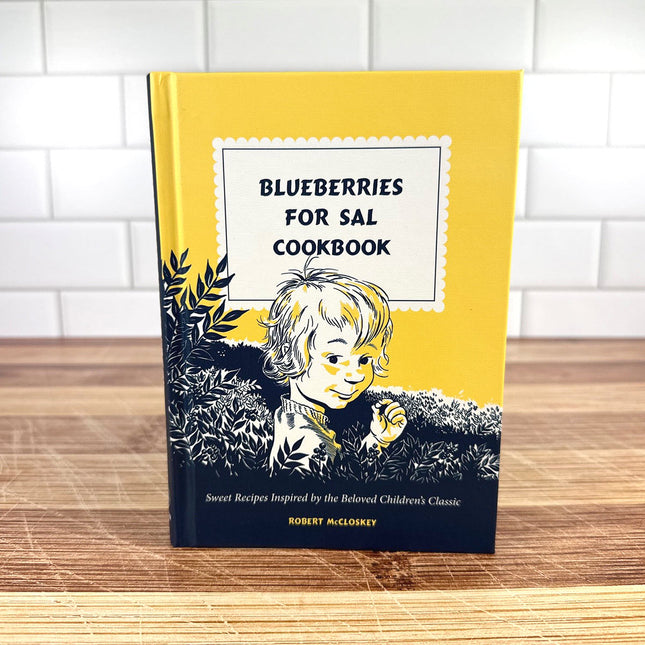 Cookbook titled 'Blueberries for Sal' on a wooden surface with a white tiled wall background