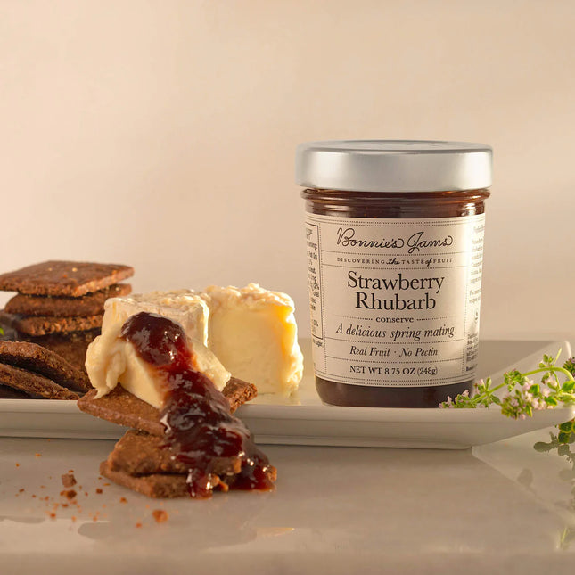Jar of strawberry rhubarb jam on a plate with crackers and cream cheese.