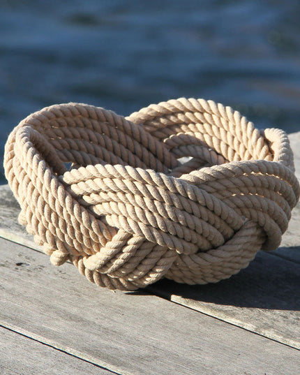 a hand woven cotton rope bowl in tan resting on a dock with a view of the water