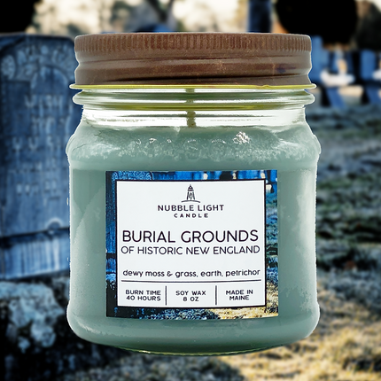 Jar of 'Burial Grounds of Historic New England' candle with a label on a blurred cemetery background