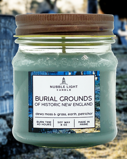 Jar of 'Burial Grounds of Historic New England' candle with a label on a blurred cemetery background