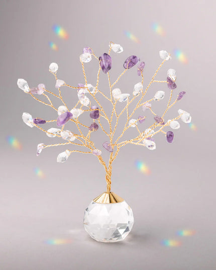 Decorative tree with gold branches and crystal base adorned with amethyst and clear crystals casting tiny rainbows against the light gray background