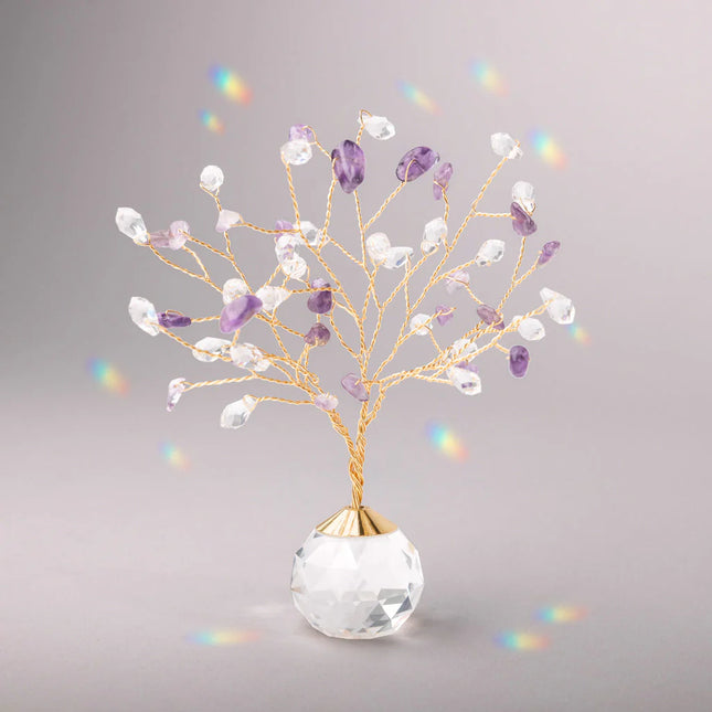 Decorative tree with gold branches and crystal base adorned with amethyst and clear crystals casting tiny rainbows against the light gray background