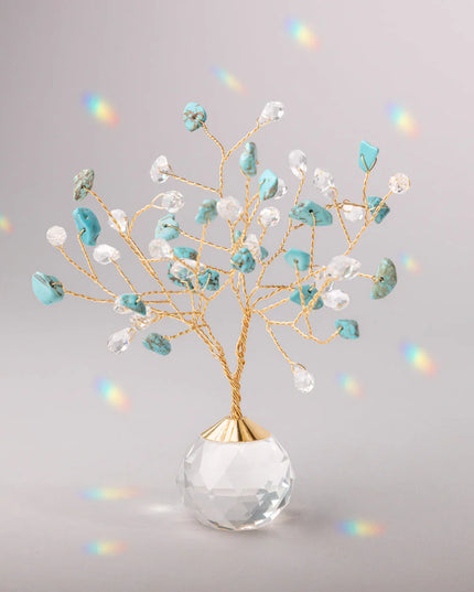 Decorative tree with gold branches and crystal base adorned with turquoise and clear crystals casting tiny rainbows against the light gray background