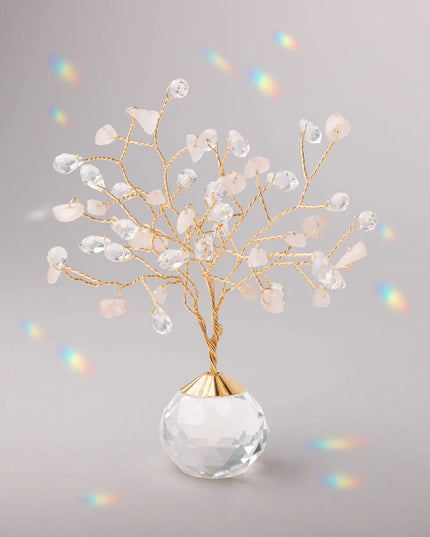 Decorative tree with gold branches and crystal base adorned with rose quartz and clear crystals casting tiny rainbows against the light gray background
