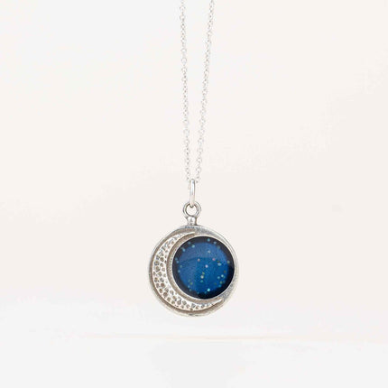 Handcrafted silver Crescent Moon Necklace featuring a stippled pendant resembling moon craters, with a sparkling blue inner section, symbolizing lunar beauty, hanging from a delicate silver chain