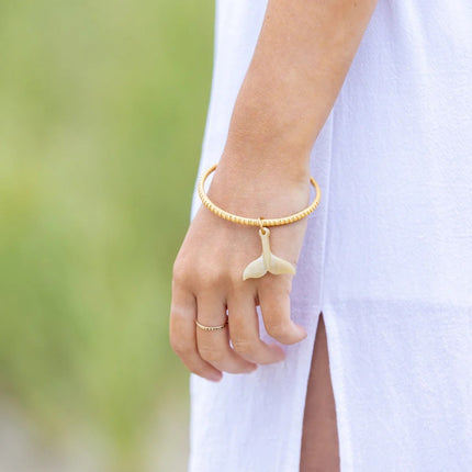 Hand with a wooden woven bracelet with a whale tail charm against a blurred green background
