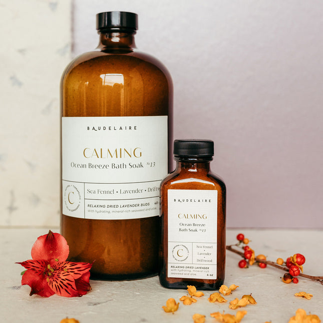 a large 40 ounce bottle of the Ocean Breeze soak alongside a small 4 ounce bottle of the spring blossom soak on a table surrounded by flower petals