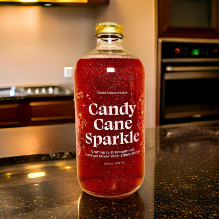 A bottle of 'Candy Cane Sparkle' cranberry and spicedew cocktail mixer with edible glitter, set on a dark kitchen countertop with a blurred kitchen background.