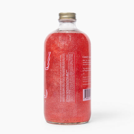A clear glass bottle filled with sparkling pinkish-red liquid, shown from the back against a clean white background. The bottle has a gold screw cap and a white label with text, though the text is not fully legible.
