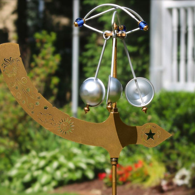an outdoor picture of A decorative wind chime featuring a copper-colored tree of life design with dangling chimes that are wind propelled.