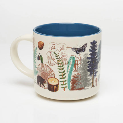 a white coffee mug with vintage illustrations of woodland flora and fauna wrapping around it, and a solid deep blue print on the inside of the mug