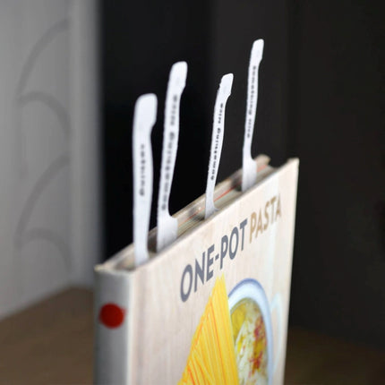 Set of knife page markers inserted in a 'One-Pot Pasta' cookbook on a dark background