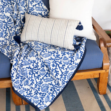 Blue and white shell and coral throw blanket draped over a wooden chair with striped flooring.