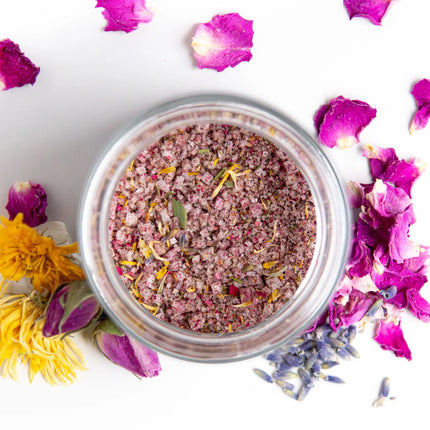 an above jar view into the flower salt jar showing colorful pink tinged salt with bits of botanicals mixed in, jar is surrounded by flower petals